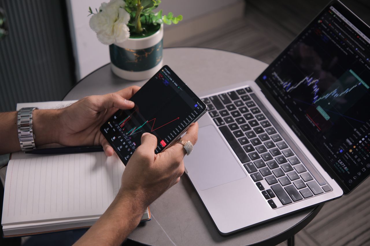 Mastering the First Impression: Your intriguing post title goes here Man analyzing stock trends with laptop and mobile trading app at a modern workspace.