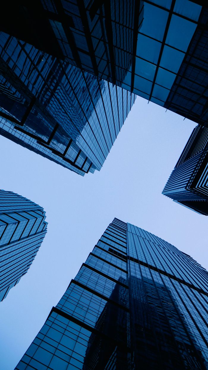 Usługi Low angle view of sleek, modern skyscrapers with glass facades forming geometric pattern against the sky.